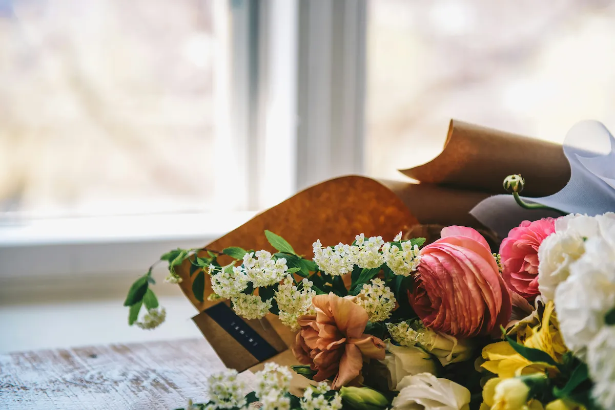 A wrapped bouquet of flowers resting on a table by a window